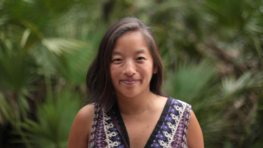 OneBeat co-director Elena Moon Park standing in front of a lush forest of tropical plants.
