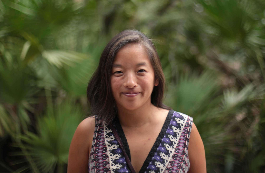 OneBeat co-director Elena Moon Park standing in front of a lush forest of tropical plants.